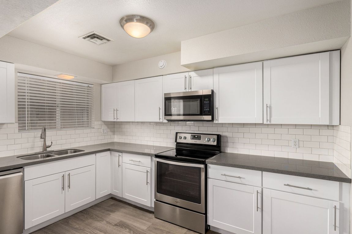White kitchen with gray countertops, stainless steel appliances, and tile backsplash.
