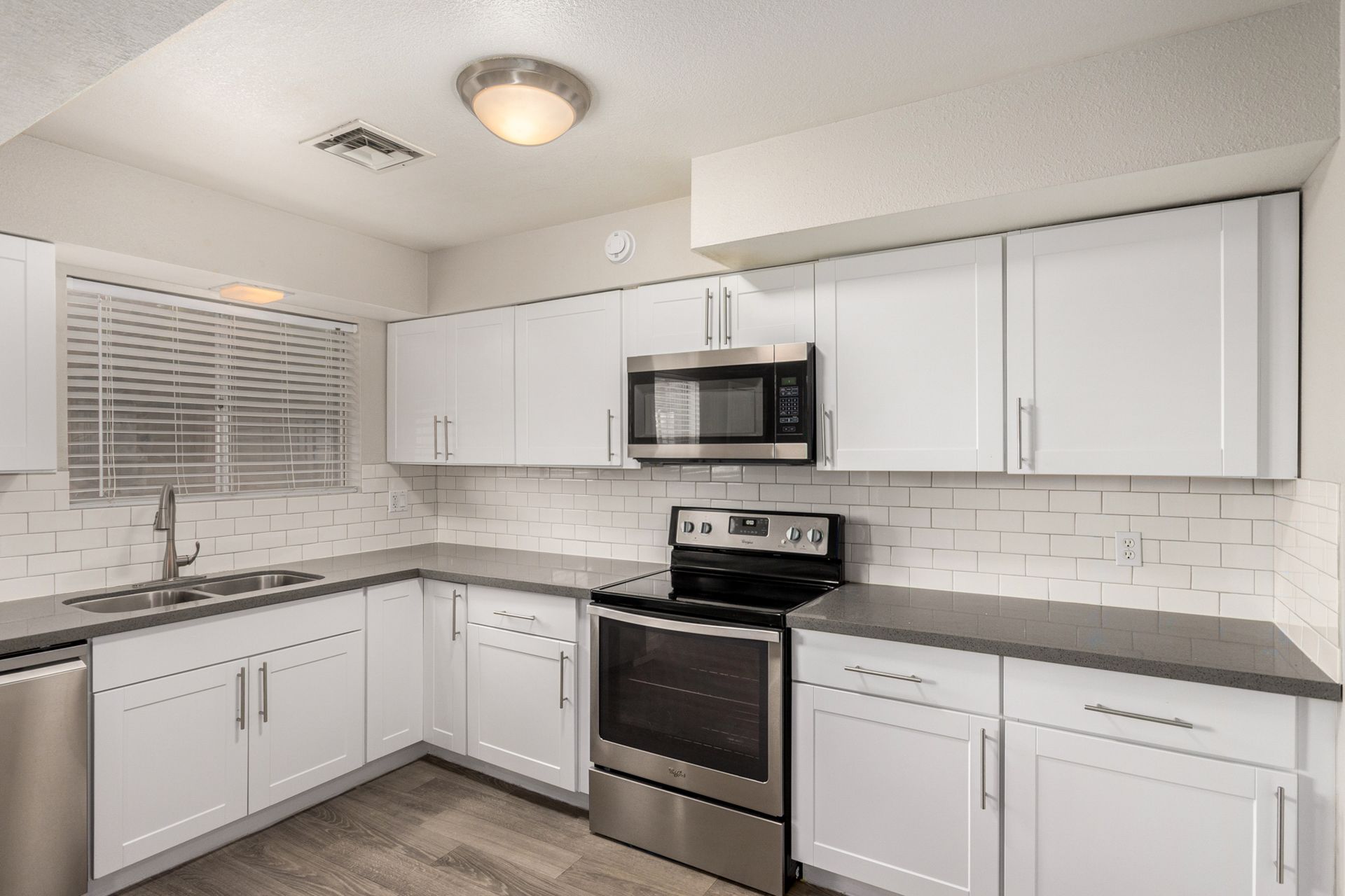 White kitchen with gray countertops, stainless steel appliances, and tile backsplash.