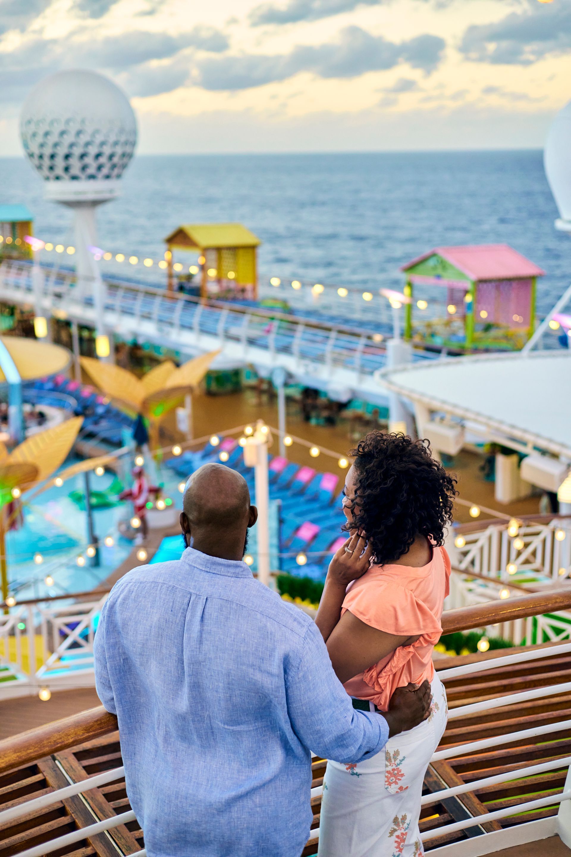 Man on Virgin Voyages cruise ship deck watching sunset over pool and lounge area