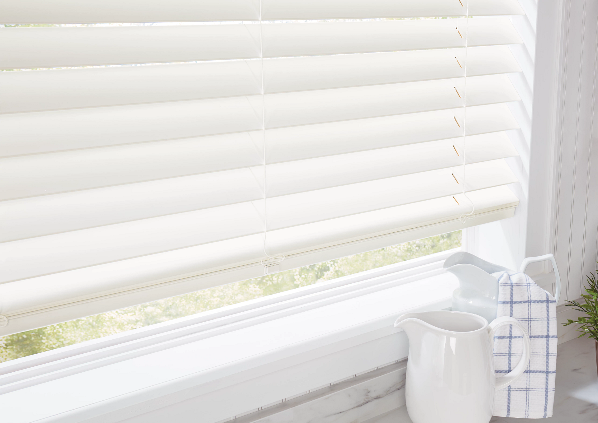 White window blinds beside a windowsill with a white mug and checkered utensil holder