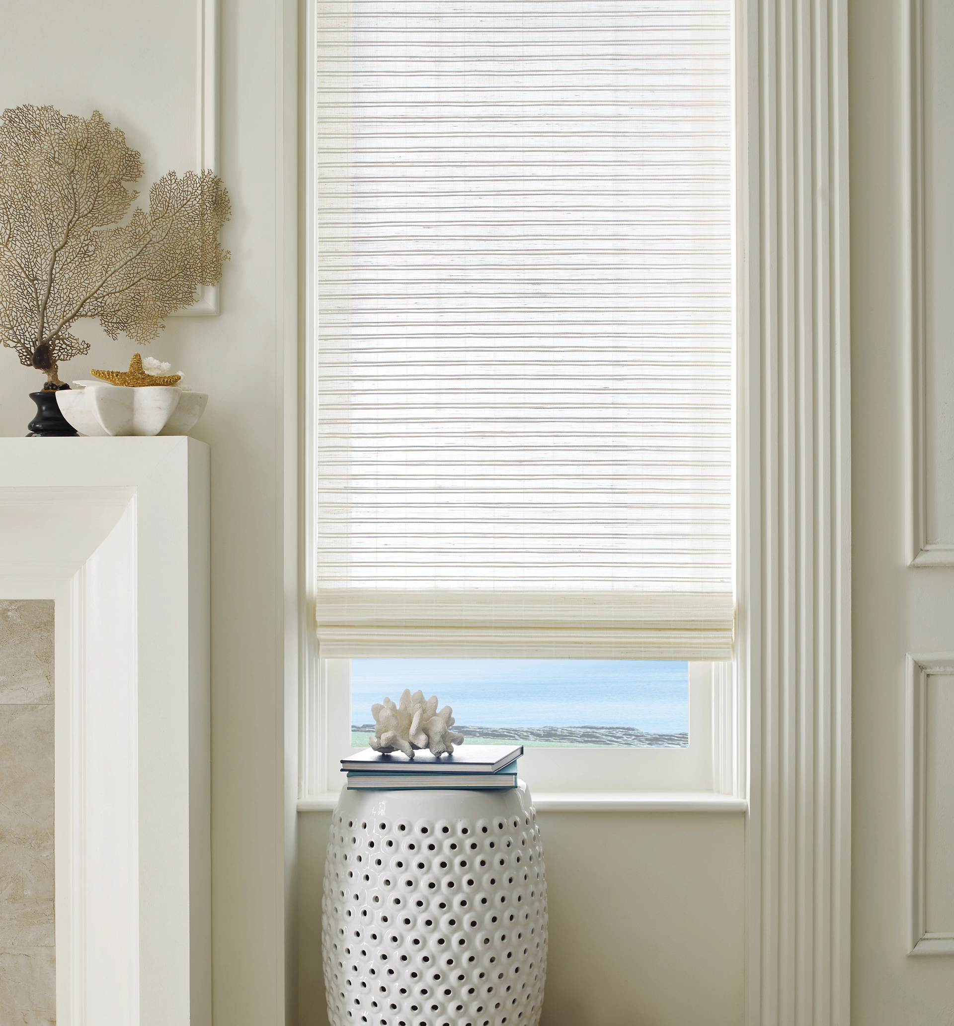 Bright window with white woven shade and a decorative ceramic stool in a light-toned room