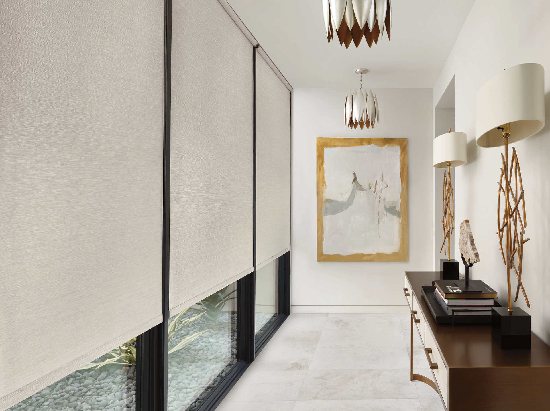 Modern hallway with cream walls, black-trimmed windows, gold-framed art, and dark wood console tables