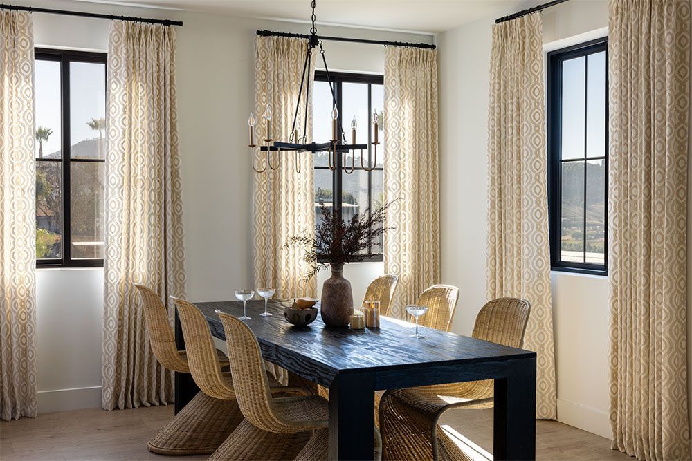 Bright dining room with blue table, wicker chairs, and patterned curtains by large windows