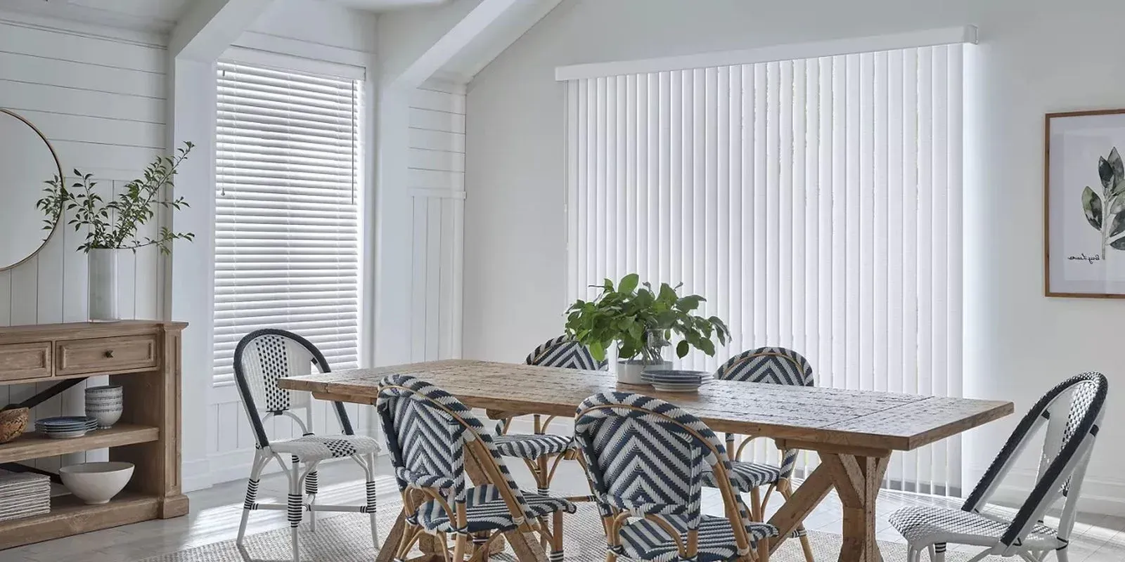 Bright dining room with a wooden table, woven chairs, large windows, and potted plants