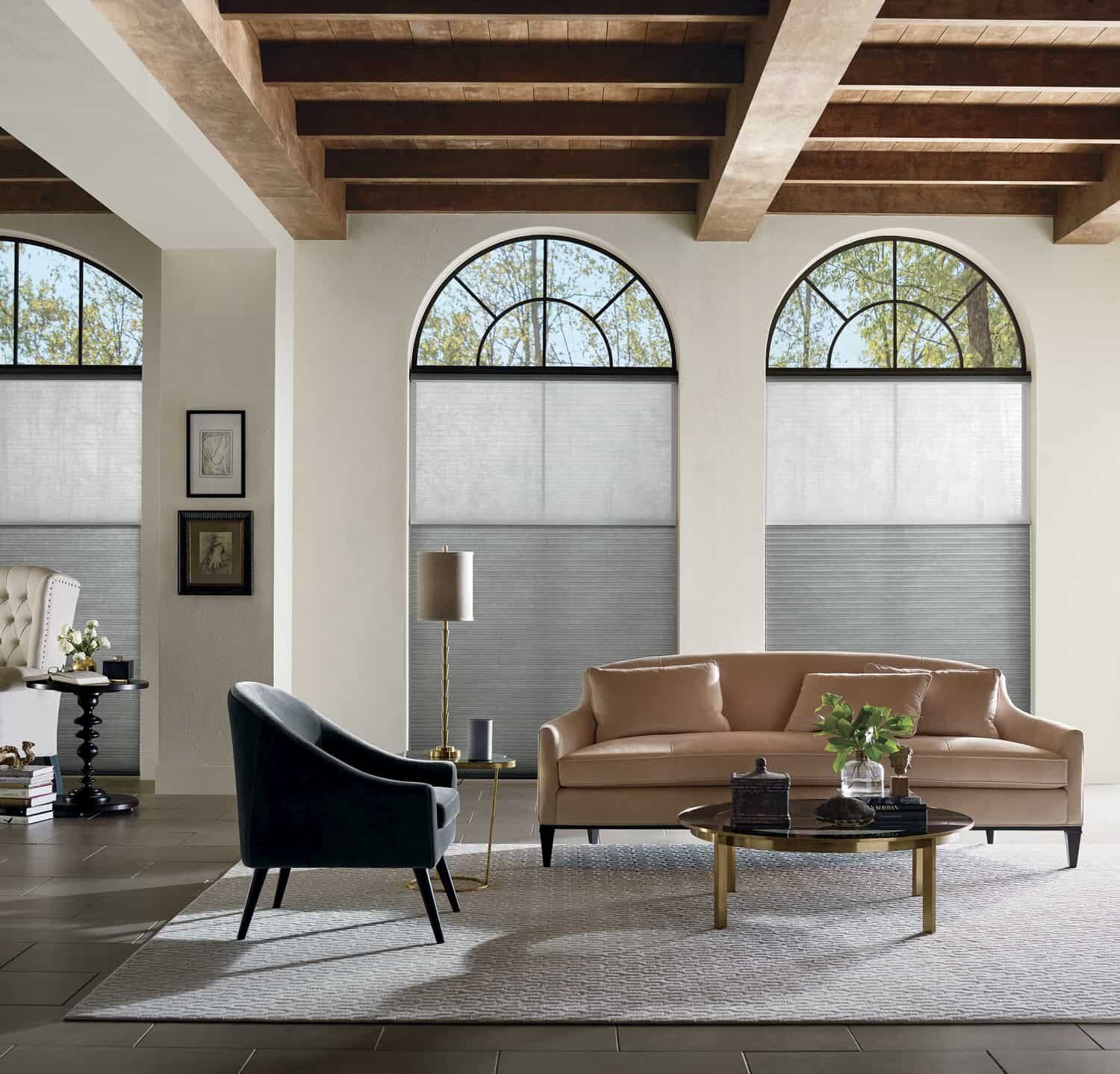 Modern living room with arched windows, tan sofa, black chair, coffee table, and exposed wood ceiling