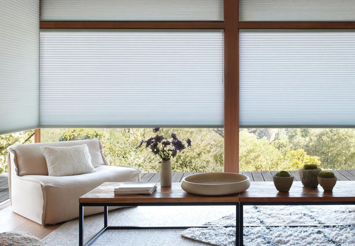 Cozy living room with beige sofa, coffee table, vase of flowers, and large windows with blinds