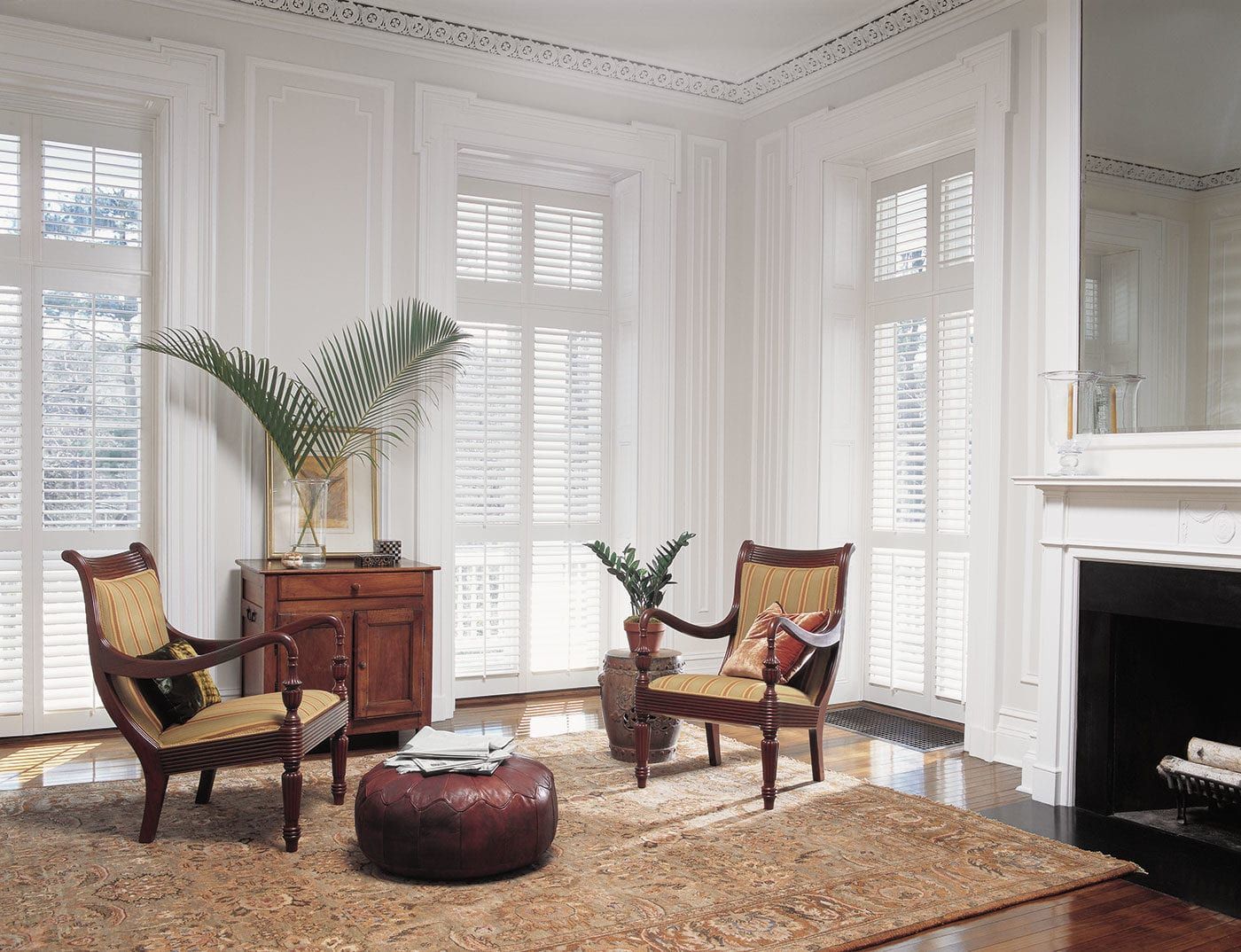 Bright living room with white shutters, wicker chairs, plants, and a fireplace on the right.