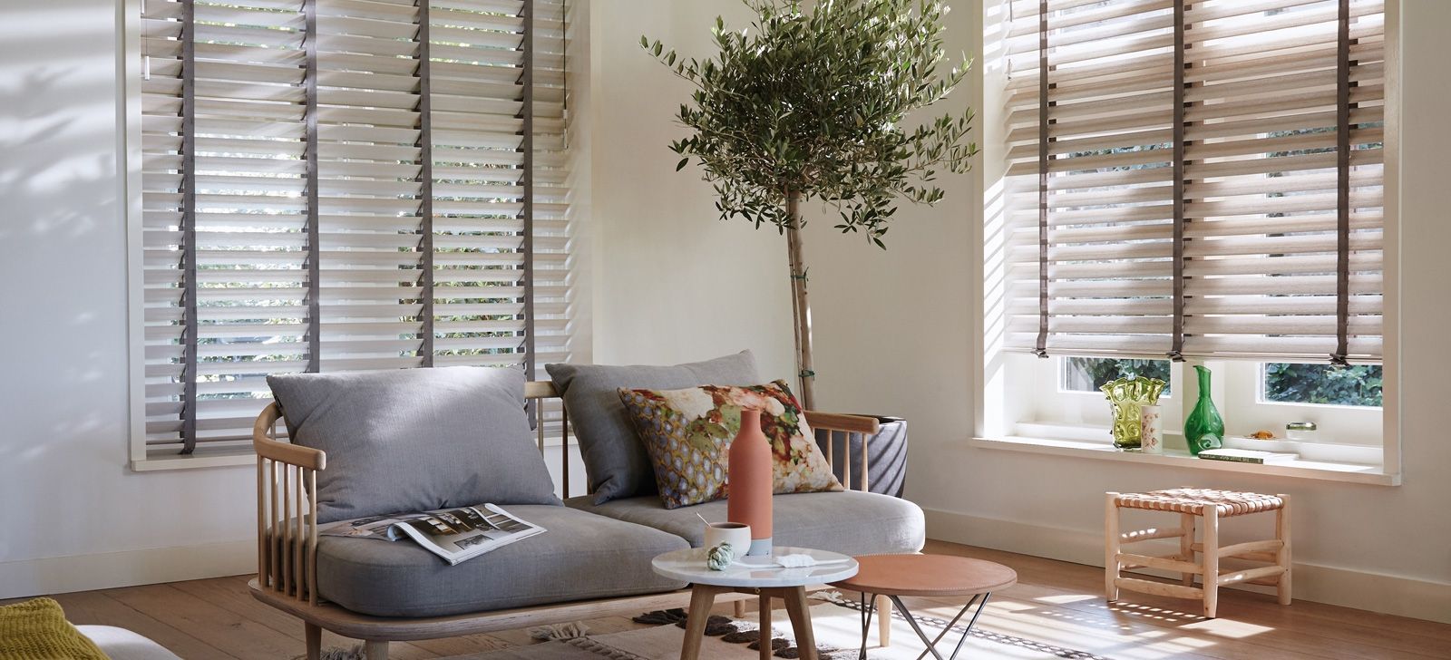 Bright living room with gray sofa, wood blinds, and a small table by a sunlit window