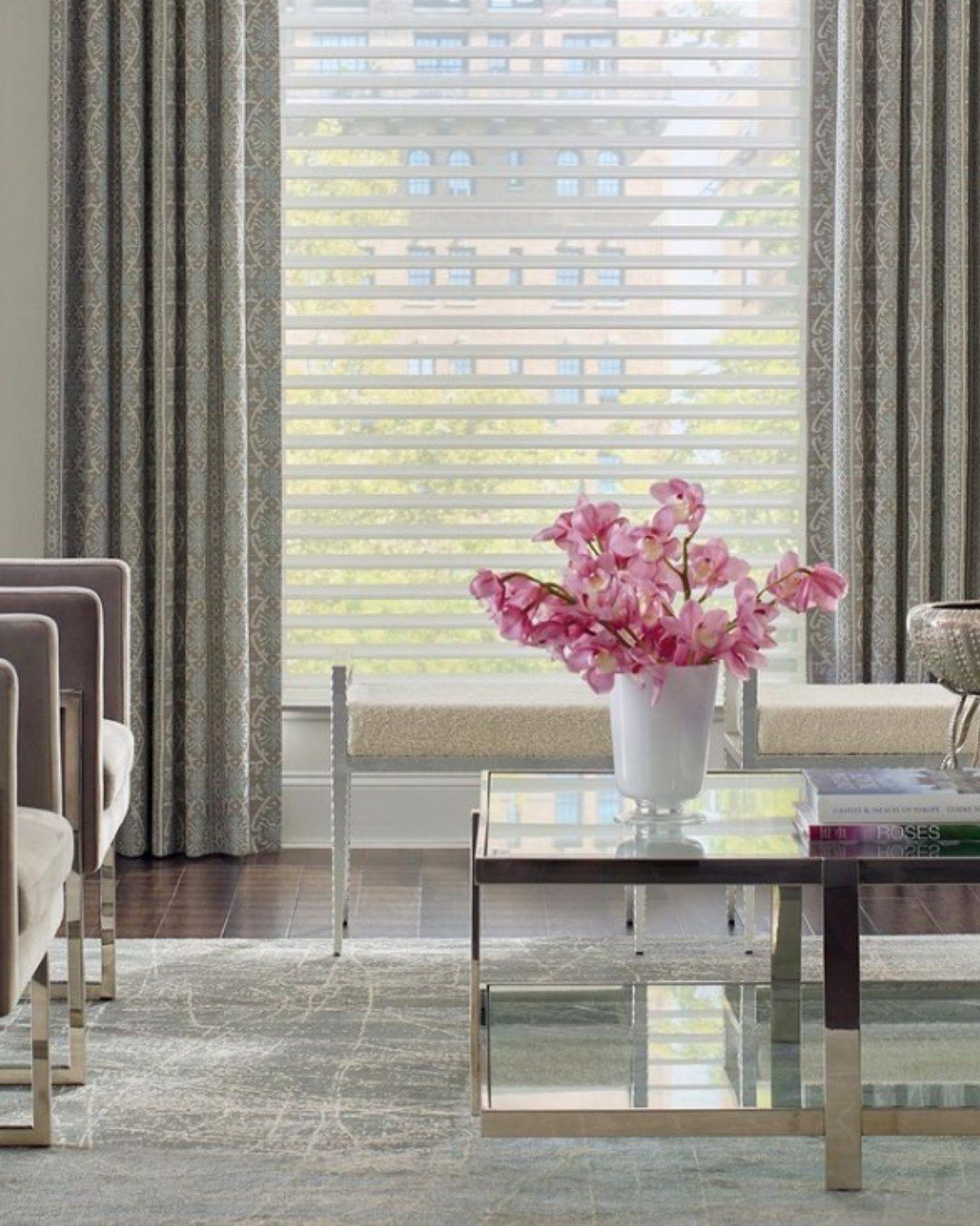 Modern living room with large window, gray curtains, and a coffee table with pink flowers.