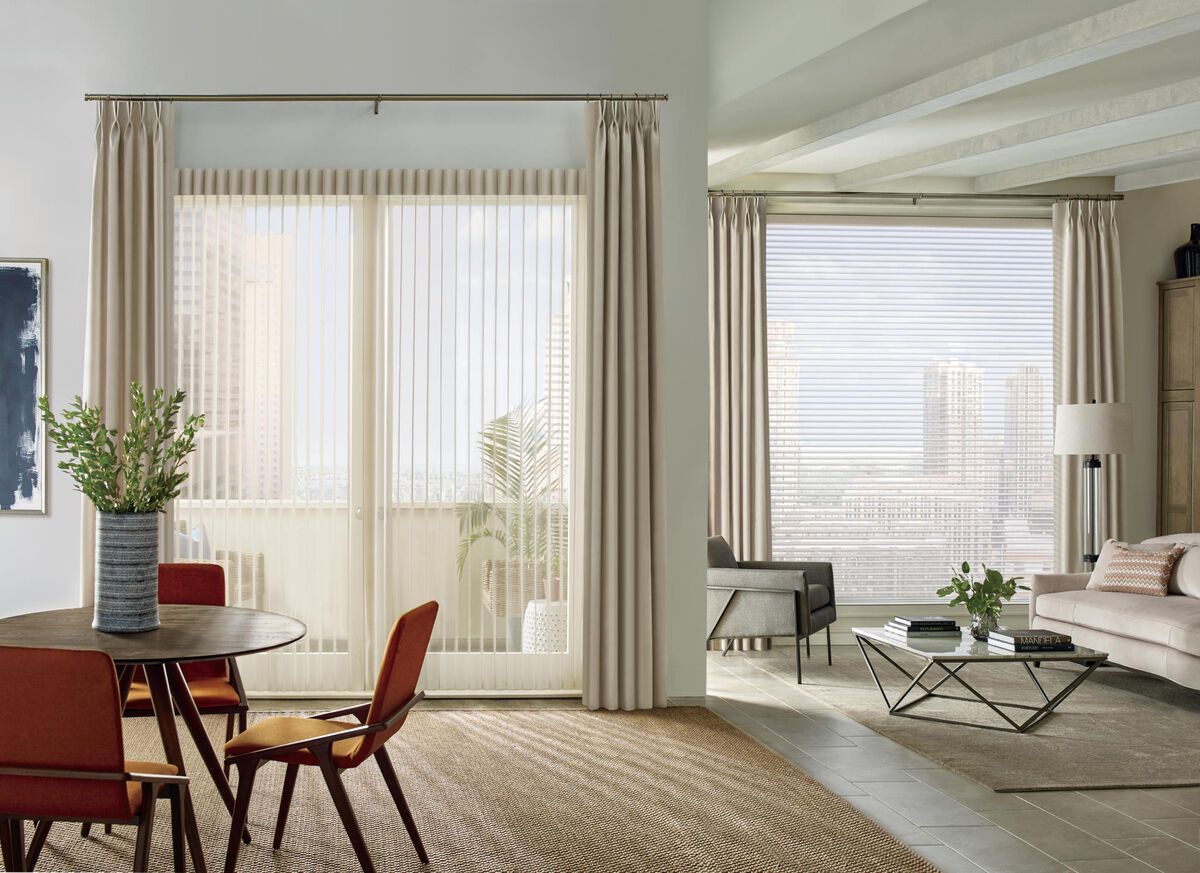 Bright living-dining room with large windows, sheer curtains, a round table, and a beige sofa