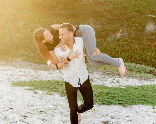 A man is carrying a woman on his back on the beach.