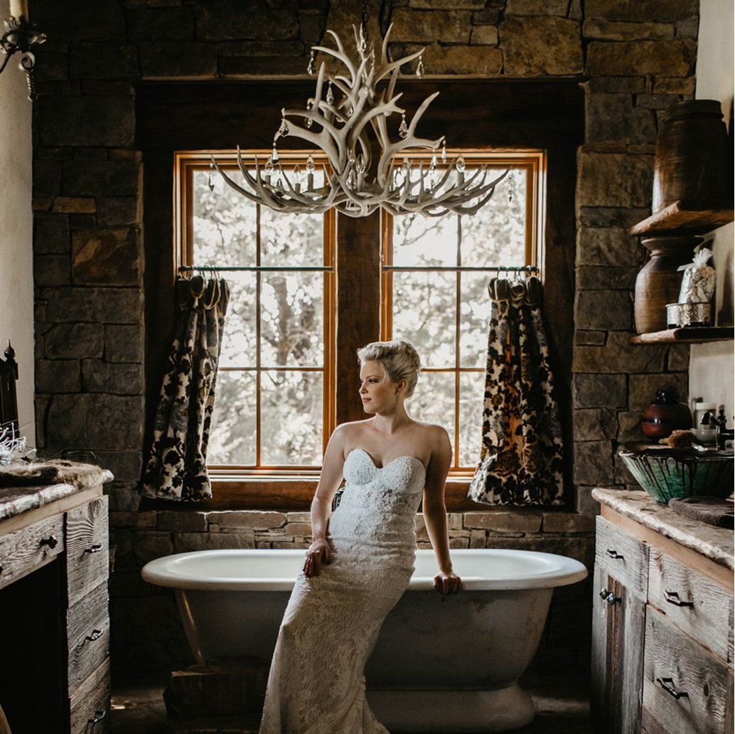woman sitting by a bathtub in a rustic house with an antler chandelier by antlerworx