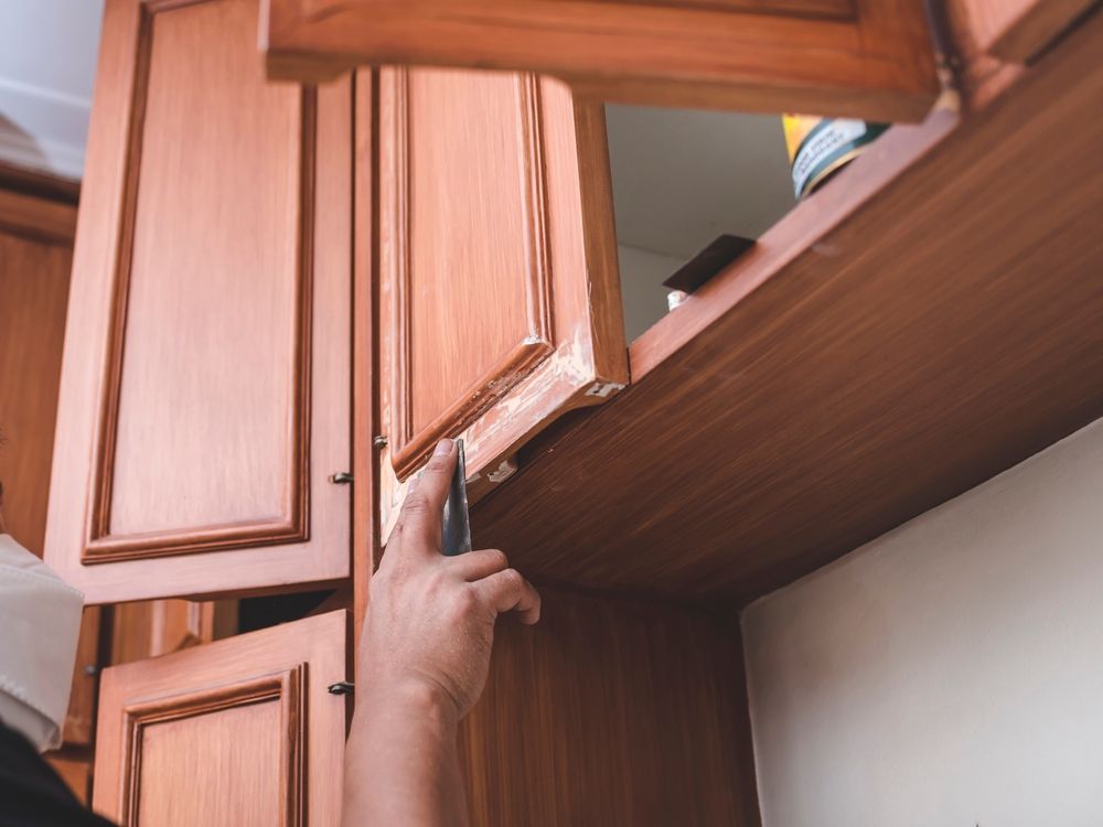 Person using a tool to repair a wooden cabinet door in a kitchen.