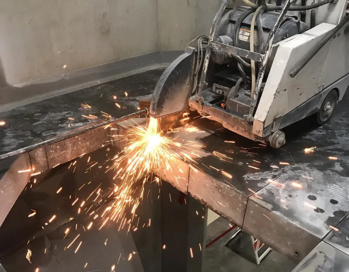 A walk-behind saw cuts through a concrete slab, producing a bright spray of sparks at the point of contact.
