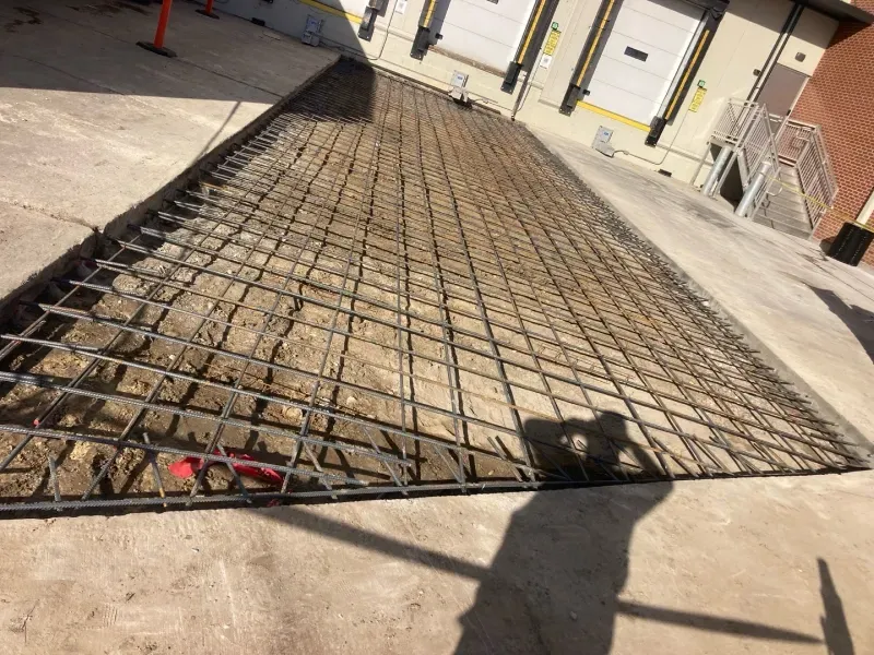 A construction site showing a grid of steel rebar laid out over dirt in preparation for a concrete pour.