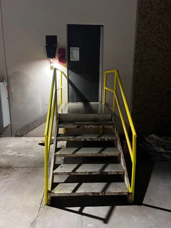 A metal stairway with yellow handrails leading to an elevated dark door on a building exterior at night.