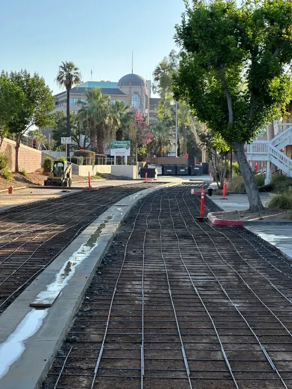 A construction site with metal rebar grid laid on the ground, preparing for a concrete pour in a suburban area.