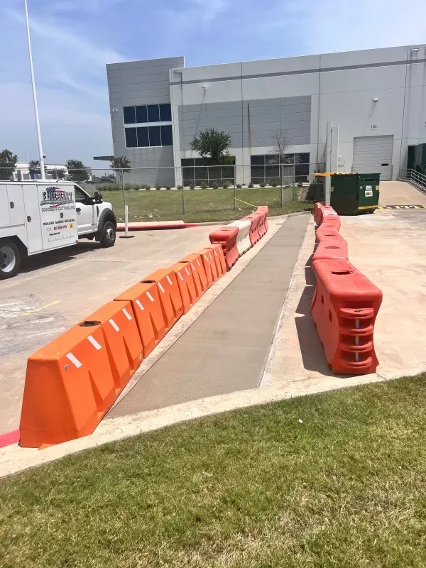 A service truck parked near a warehouse, with orange plastic barriers creating a pedestrian walkway on the asphalt.