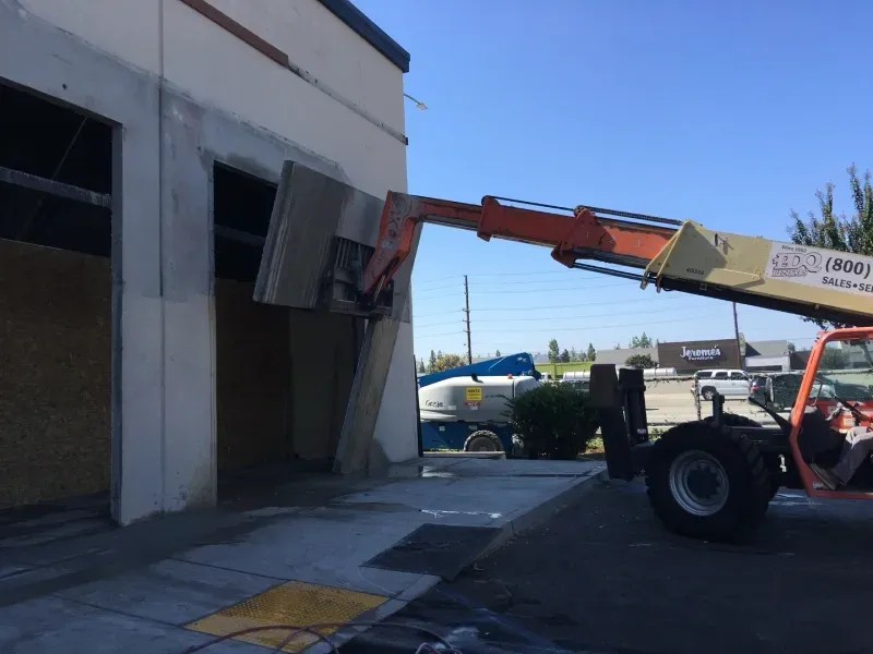 An orange telescopic forklift lifting a concrete panel into a doorway of a building.