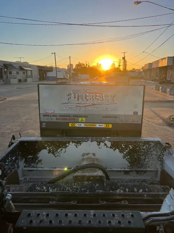 View of a piece of industrial equipment, possibly a parts washer, against a vibrant orange sunset over a city street.