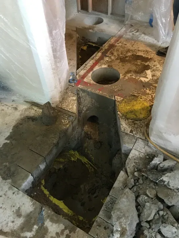 A construction site floor showing a rectangular trench, a circular pipe hole, and debris on a concrete surface.