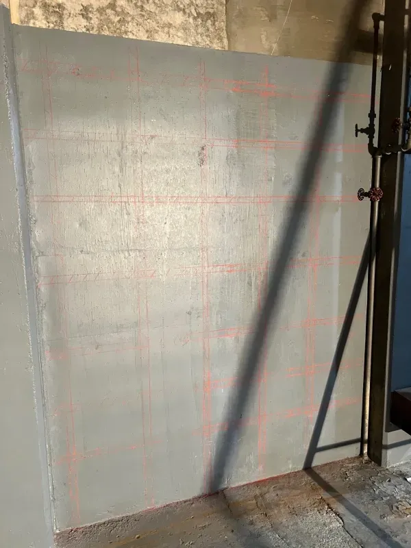 A gray wall marked with a red grid pattern, positioned next to a dark metal pipe structure.