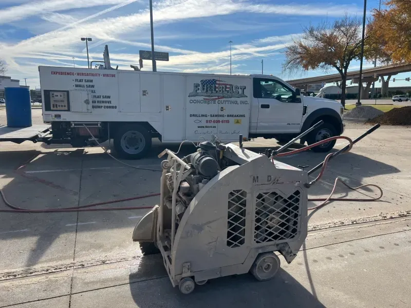 A beige concrete saw sits on a paved lot in front of a white work truck from 