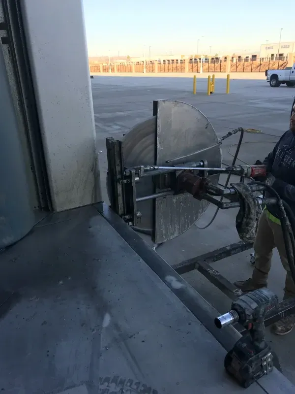 A person operating a large, circular wall saw against a concrete structure outdoors.