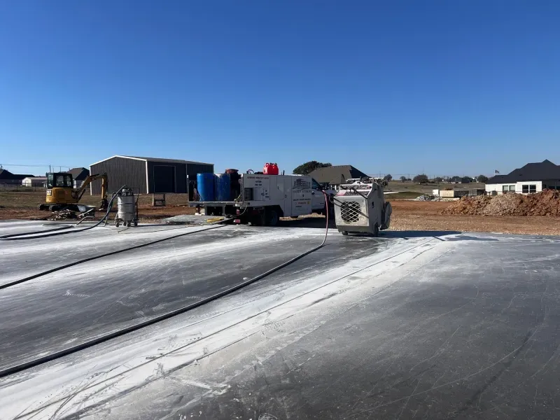 Construction equipment and a work truck on a paved site covered with white powder under a clear blue sky.