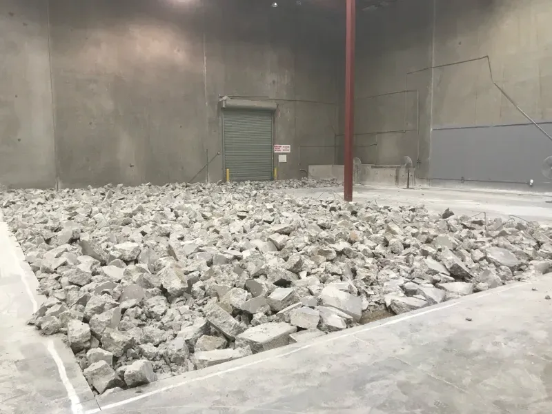 A large, indoor industrial warehouse space with a section of the concrete floor broken up into a pile of rubble.