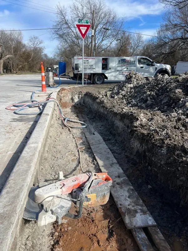 Construction zone with a concrete saw, a trench, a service truck, and a yield sign under a blue sky.