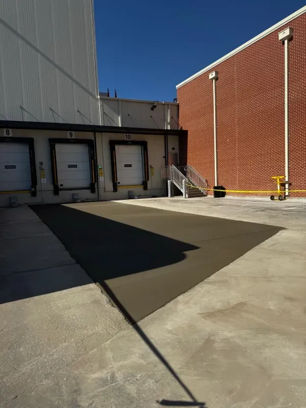 Loading docks with a freshly poured, dark concrete rectangular patch in front of the bay doors against a brick building.