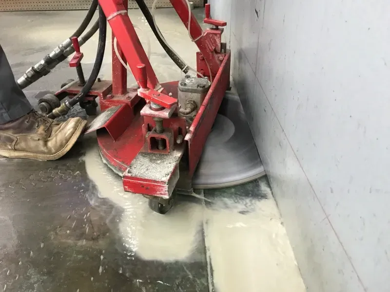 A red saw cuts into a concrete floor against a wall, producing a grey slurry.