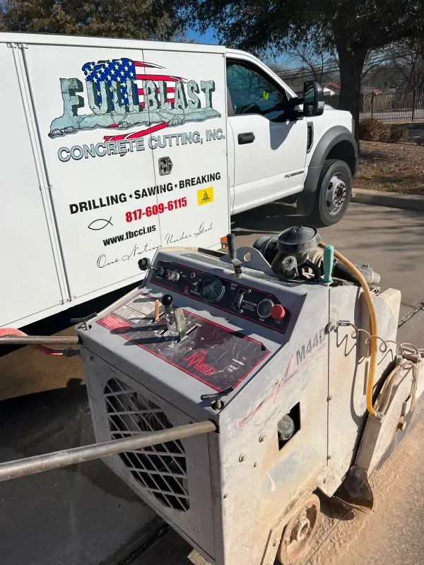 A walk-behind concrete saw sits in front of a white Fullblast Concrete Cutting work van parked on an asphalt lot.