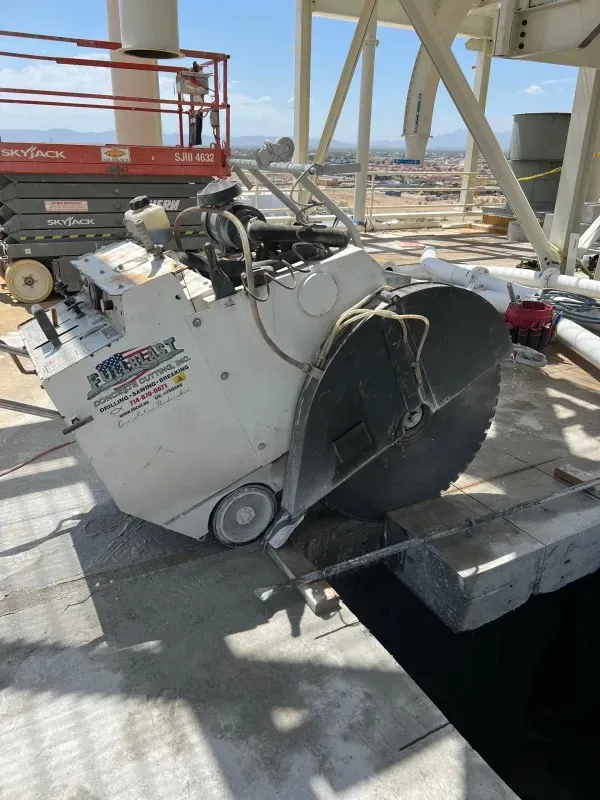 A large, white industrial concrete saw with a black blade sits on a construction site next to a hole in the floor.