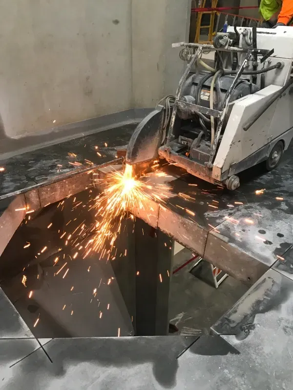 A floor saw cuts through a concrete slab, creating a bright spray of sparks in an indoor construction setting.