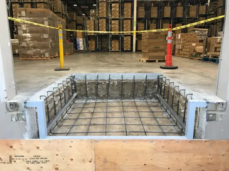 A rectangular recessed loading dock pit in a warehouse floor, featuring exposed rebar framing and a metal edge form.