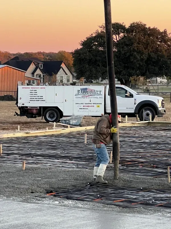 A construction worker uses a concrete hose to pour foundation at a job site with a utility truck parked in the background.