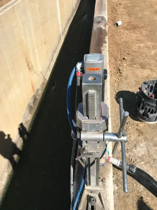 A diamond core drill mounted on a stand, positioned on a concrete edge at an outdoor construction site.