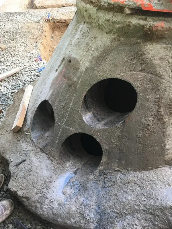 A gray, concrete structure featuring three large circular holes, likely created by core drilling, on a construction site.