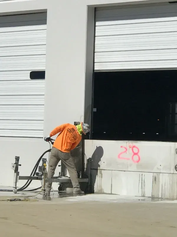 A worker in high-visibility orange clothing uses a concrete saw at a loading dock marked with the number 28.