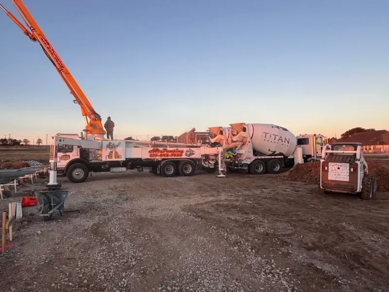 A concrete boom pump truck and a Titan mixer truck at a construction site at sunset.