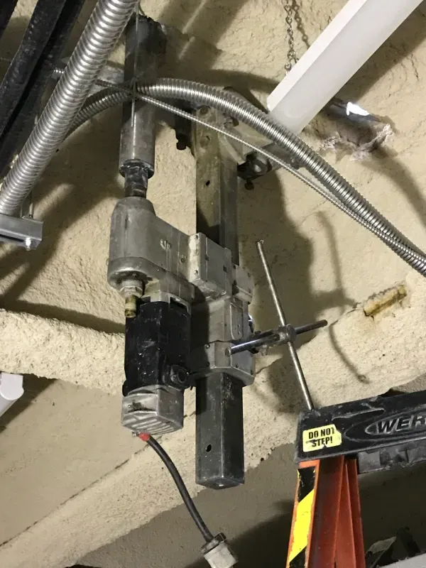 A ceiling-mounted industrial mechanical actuator with exposed wires and metal structural components.