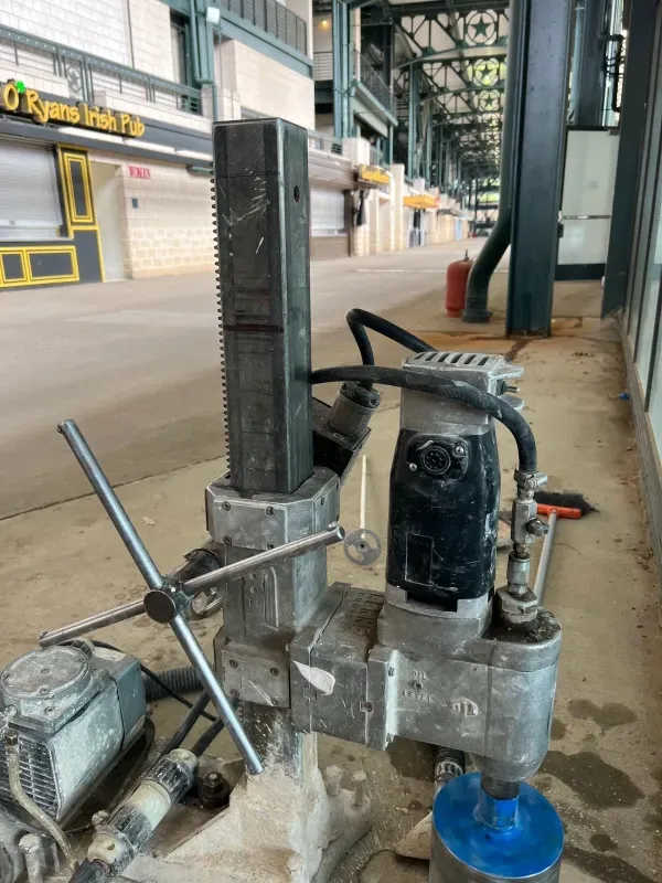 A core drill machine on a stand sits on a concrete concourse outside a closed pub at a stadium.