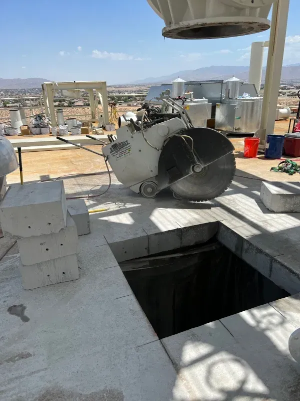 A white flat saw sits on a concrete pad next to a square cut-out in a desert industrial construction site.
