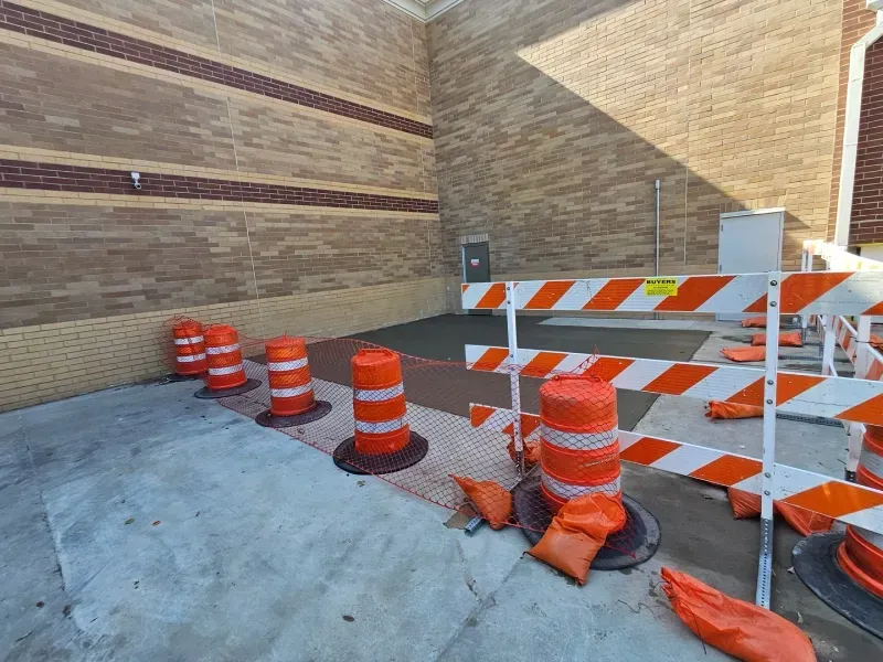 Orange traffic barrels and temporary barricades block a walkway outside a building with brick walls.