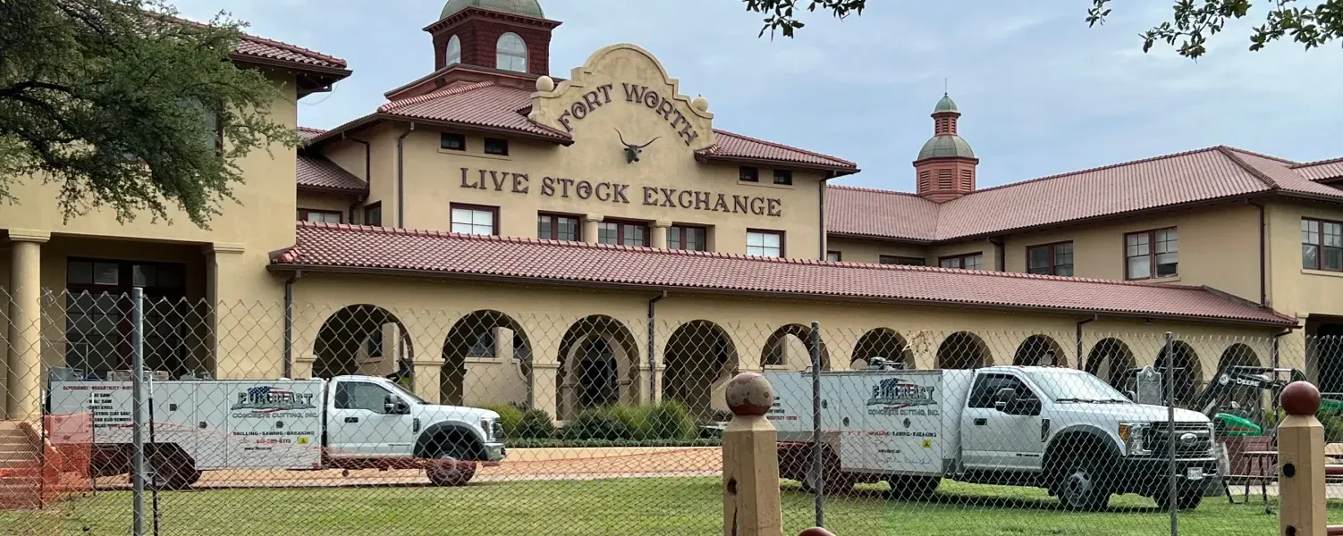 The Fort Worth Stockyards Live Stock Exchange building featuring tan stucco, arched porticos, and two service trucks.