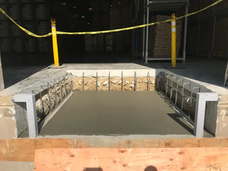 A rectangular concrete loading dock pit under construction, featuring exposed steel rebar and metal edge frames.