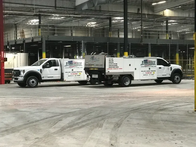 Two white utility service trucks parked side-by-side in a large, industrial warehouse space.