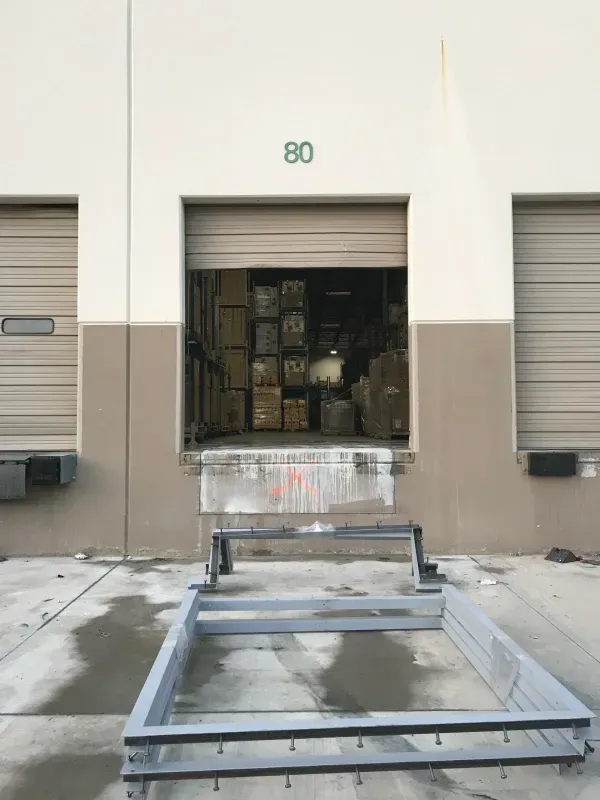 A loading dock door marked 80, with stacked boxes inside and metal industrial frames resting on the concrete ground.